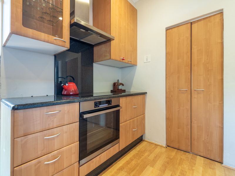 Compact kitchen featuring light wood cabinetry, granite countertops, integrated oven and hob, and a convenient built-in pantry cupboard.