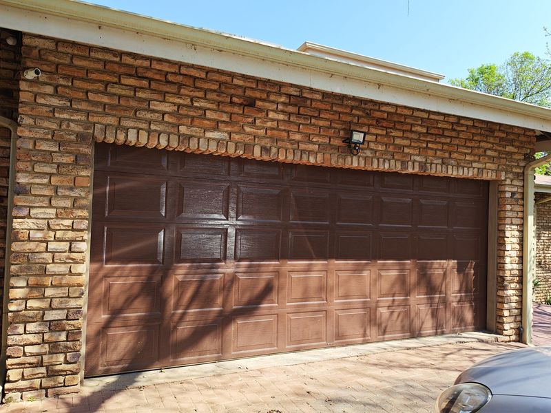 A double garage featuring a brown sectional door set within a classic face-brick facade, complete with exterior security lighting and a paved driveway.