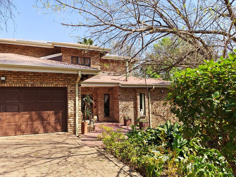 Front elevation of a face brick townhouse featuring a paved driveway, double garage, and established garden surroundings.