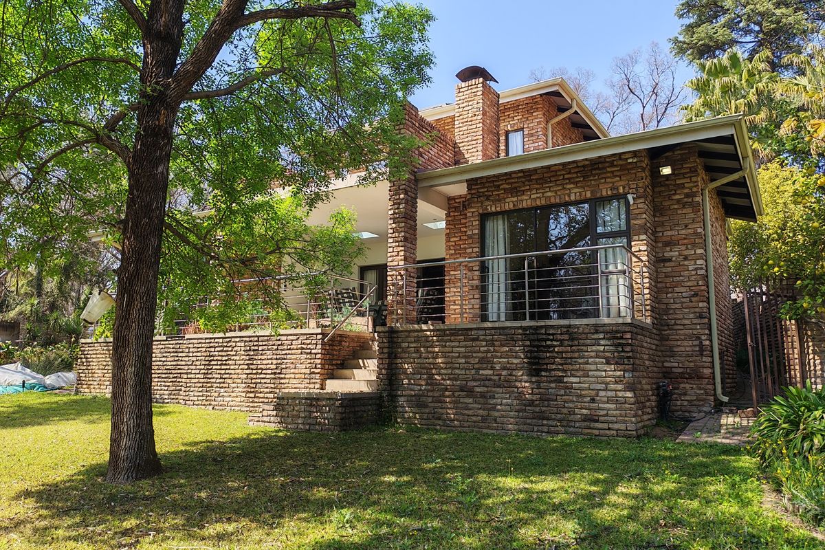 Rear view of a brick townhouse featuring a covered patio, stainless steel balustrades, and a chimney, set within a landscaped garden.