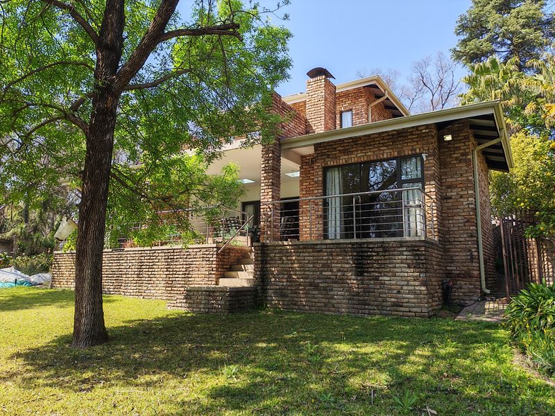 Rear view of a brick townhouse featuring a covered patio, stainless steel balustrades, and a chimney, set within a landscaped garden.