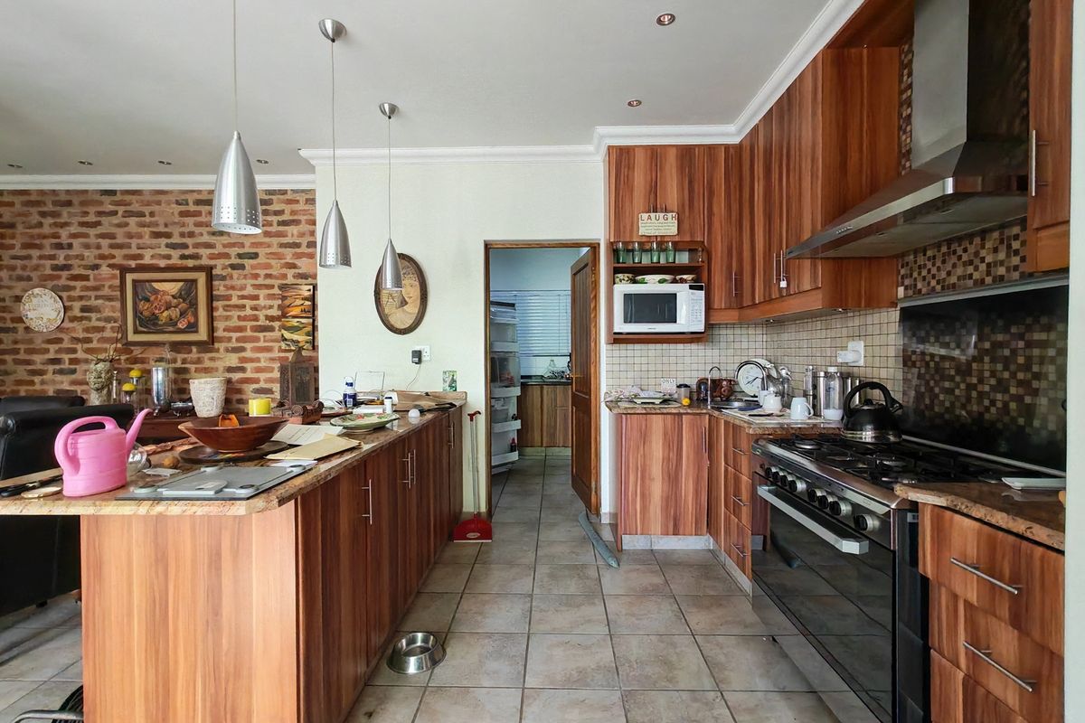 Spacious kitchen featuring wood veneer cabinetry, granite countertops, gas stove, and an exposed brick feature wall, with an adjacent scullery area.