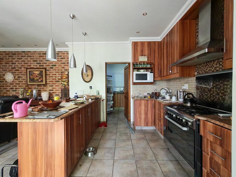 Spacious kitchen featuring wood veneer cabinetry, granite countertops, gas stove, and an exposed brick feature wall, with an adjacent scullery area.