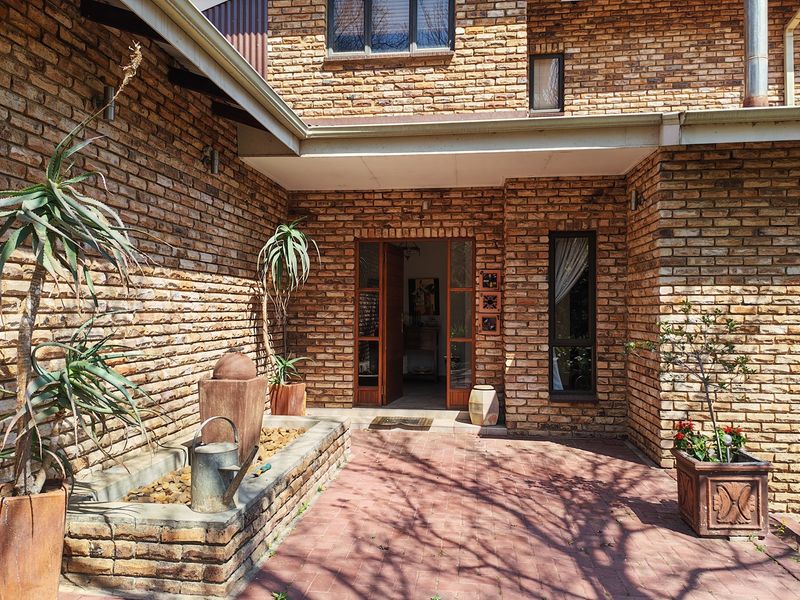 A charming brick-faced townhouse entrance featuring a paved patio area and a built-in water feature, leading to a timber-framed glass front door.