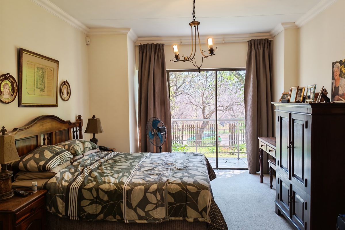 A well-lit bedroom featuring carpeted flooring, decorative cove cornicing, a central chandelier, and a sliding glass door providing access to an outdoor balcony.