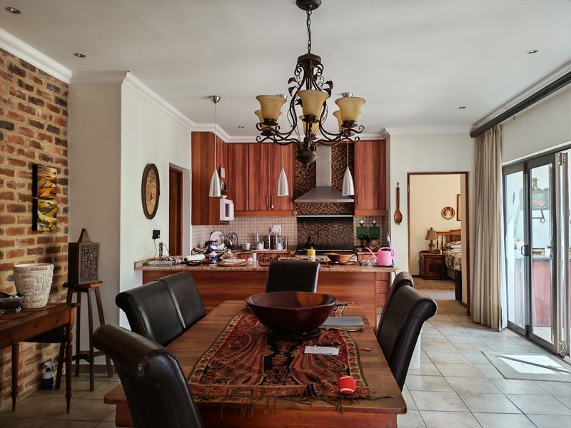 Open-plan living and dining area featuring a kitchen with wooden cabinetry, granite countertops, exposed brick accents, and direct access to an outdoor patio.