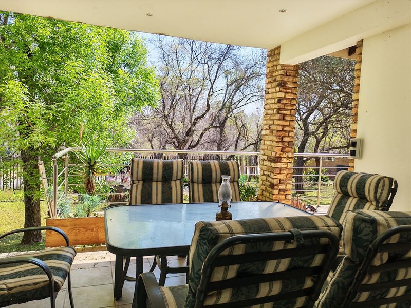 A covered patio featuring a brick pillar, stainless steel balustrade, and recessed downlights, overlooking a garden area.