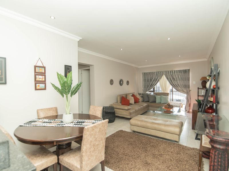 An open-plan living and dining area featuring tiled flooring, recessed downlighting, and a sliding glass door providing access to the balcony.