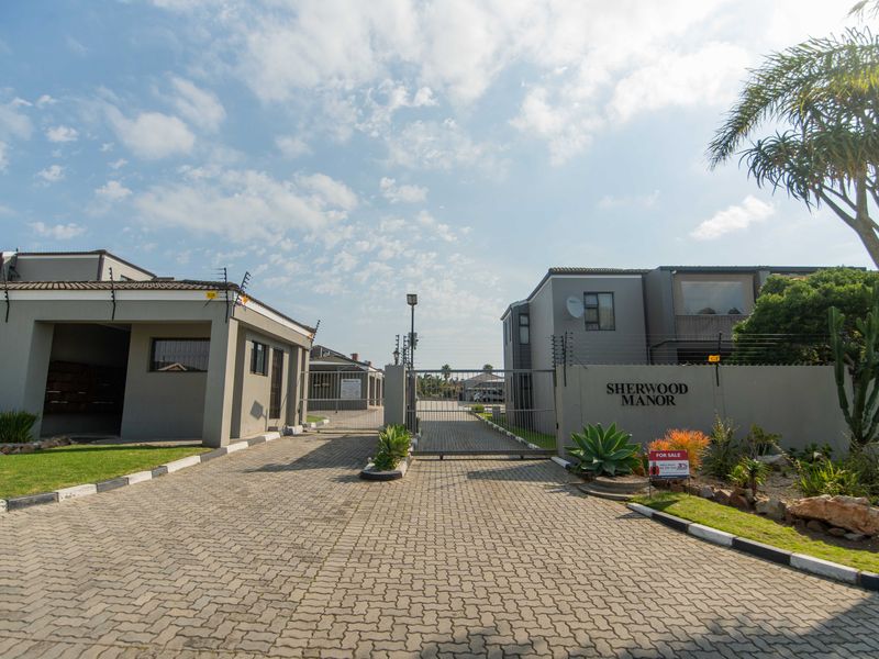 Front entrance view of Sherwood Manor complex featuring a paved driveway, secure gated access, and perimeter electric fencing.