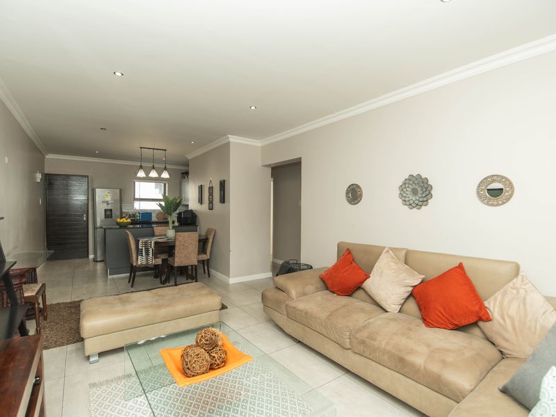 An open-plan living and dining area featuring tiled flooring, recessed downlighting, and a functional kitchen island layout.
