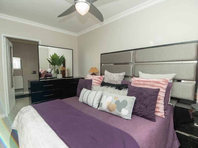 A well-maintained bedroom featuring crown molding, a ceiling fan, and tiled flooring, with an adjoining view into a bathroom.