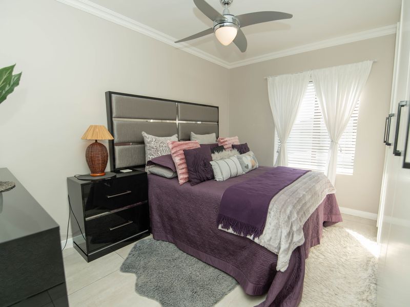 A well-maintained bedroom featuring tiled flooring, crown molding, a ceiling fan, and built-in wardrobe storage.