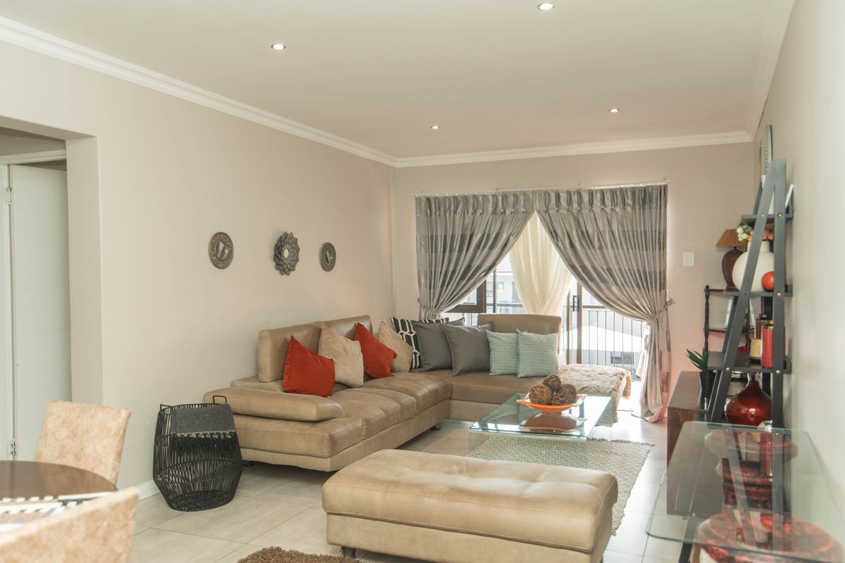 A well-maintained living room featuring neutral tiled flooring, recessed downlighting, and a sliding glass door providing access to an outdoor area.