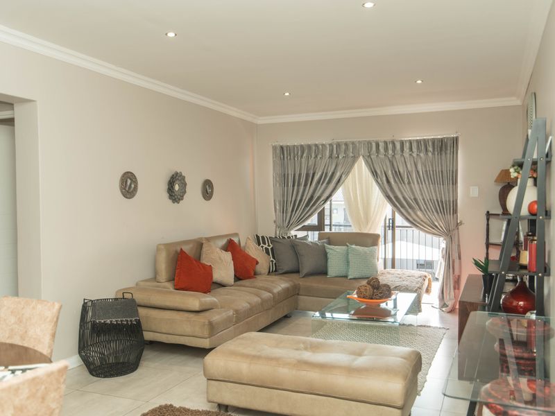 A well-maintained living room featuring neutral tiled flooring, recessed downlighting, and a sliding glass door providing access to an outdoor area.
