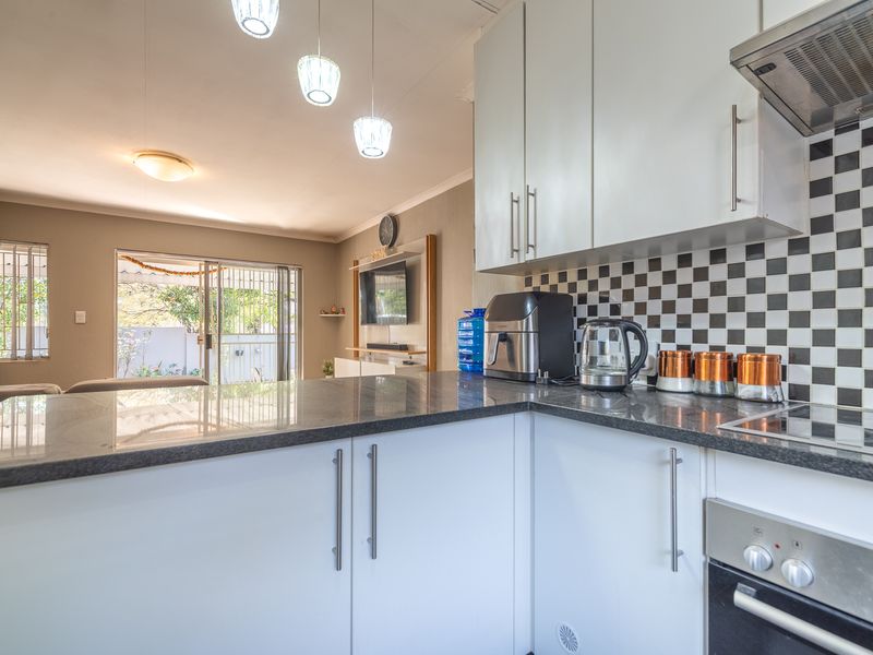An open-plan kitchen and living area featuring modern white cabinetry, granite countertops, a checkered backsplash, and direct access to an outdoor patio.