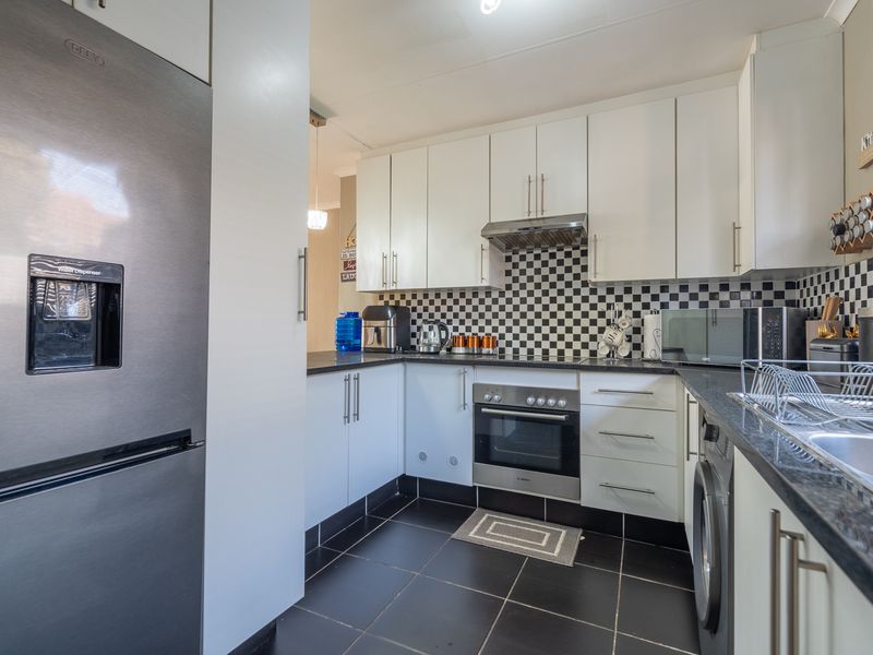 A functional kitchen featuring white cabinetry, black granite countertops, a tiled checkerboard splashback, and integrated oven with extractor fan.