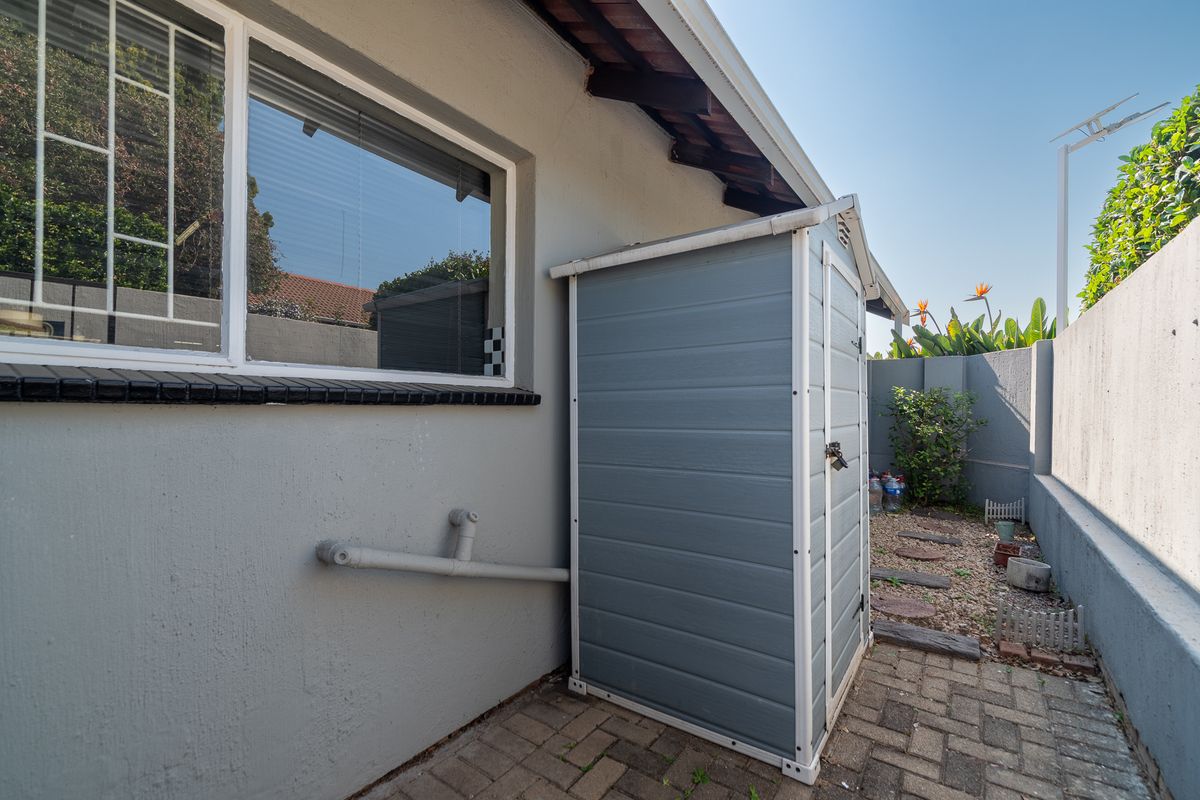 A side courtyard area featuring paved flooring, a boundary wall, and an external storage unit against the townhouse exterior wall.
