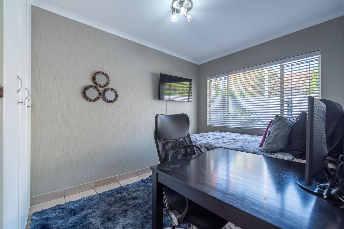 A functional bedroom featuring a built-in wardrobe, venetian blinds, and neutral wall finishes, suitable for use as a bedroom or home office space.
