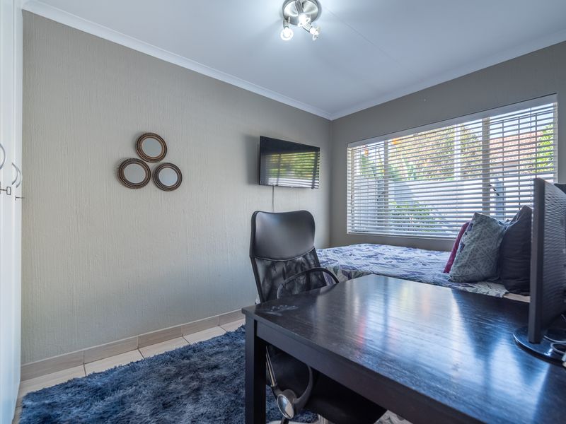 A functional bedroom featuring a built-in wardrobe, venetian blinds, and neutral wall finishes, suitable for use as a bedroom or home office space.
