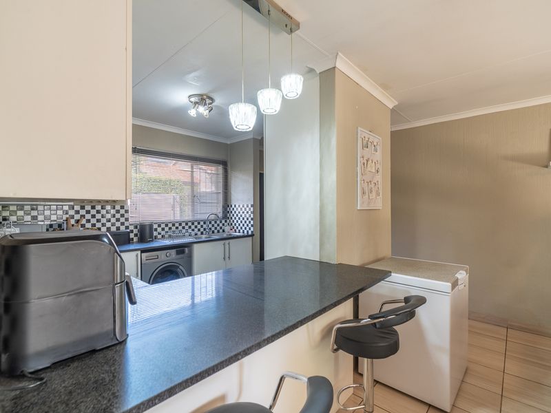 Open plan kitchen and living area featuring a granite breakfast bar, tiled flooring, and a functional kitchen layout with a checkered tile backsplash.