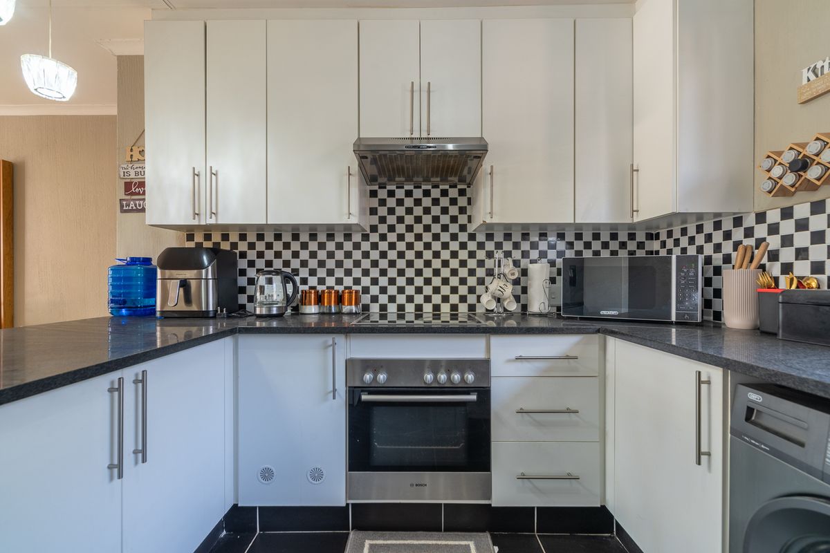 A well-maintained kitchen featuring white cabinetry, black granite countertops, a stainless steel oven with extractor fan, and a distinctive checkered tile backsplash.