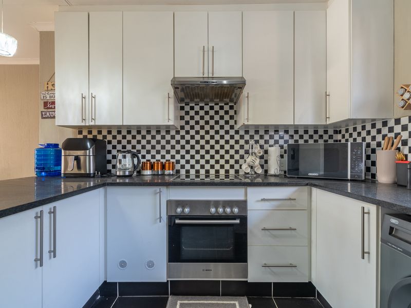 A well-maintained kitchen featuring white cabinetry, black granite countertops, a stainless steel oven with extractor fan, and a distinctive checkered tile backsplash.