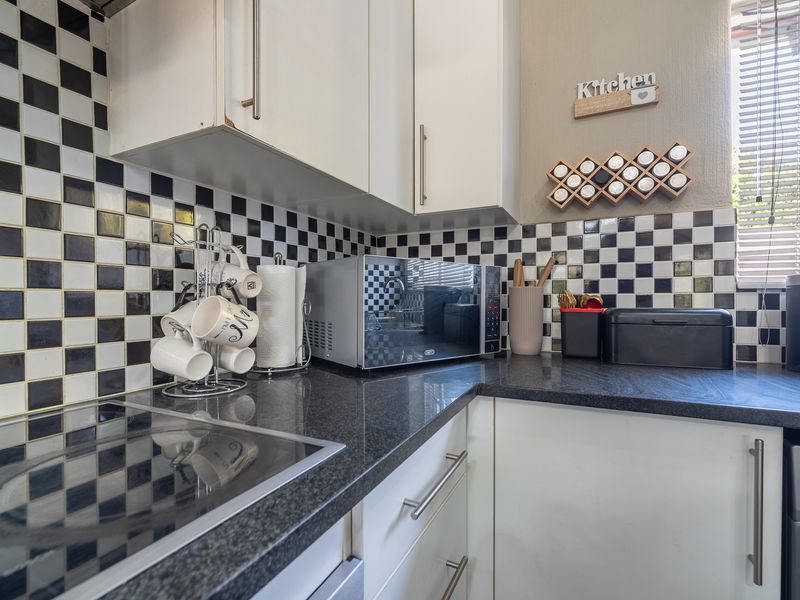 A compact kitchen featuring dark granite countertops, white cabinetry, and a distinctive black and white checkerboard tile backsplash.