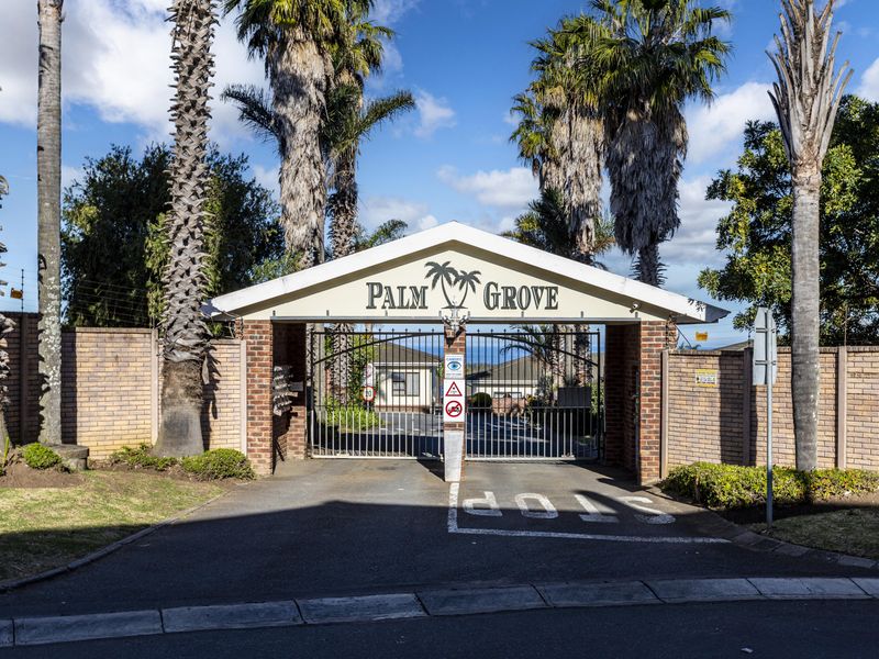 The entrance to Palm Grove estate featuring a secure gated access point with brick boundary walls and established palm trees.