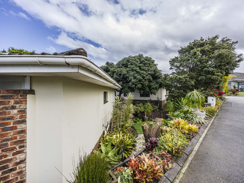 A view of the property's exterior side facade featuring brick detailing, guttering, and a well-maintained landscaped garden bordering the driveway.