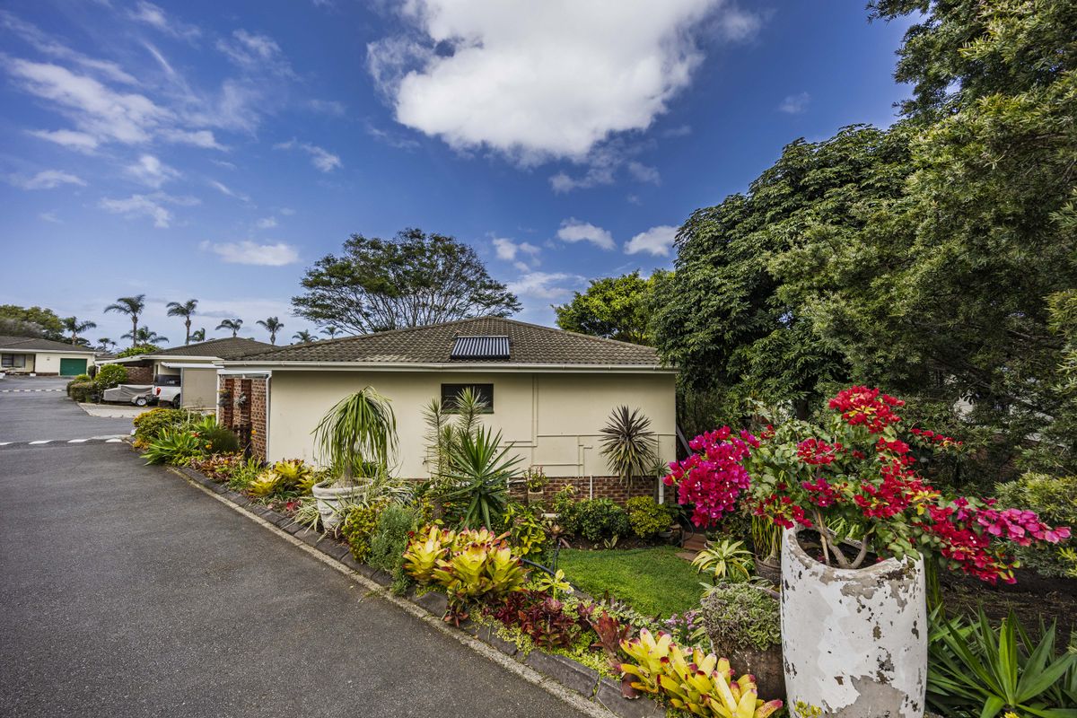 A view of the rear exterior of the property featuring a tiled roof with a solar panel, surrounded by established garden beds and a driveway.
