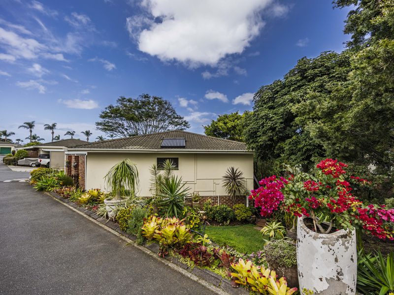 A view of the rear exterior of the property featuring a tiled roof with a solar panel, surrounded by established garden beds and a driveway.