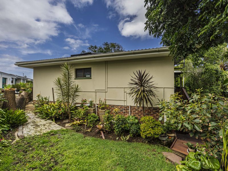 A view of the rear exterior of the house, featuring a landscaped garden, paved pathway, and timber decking area.
