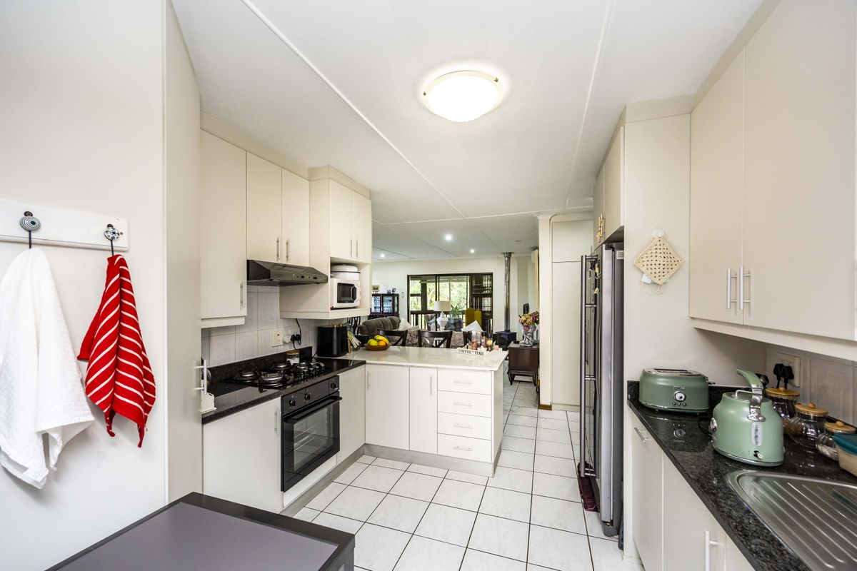 A functional kitchen featuring light-toned cabinetry, granite countertops, a gas hob, and tiled flooring, with an open-plan layout leading to the living area.