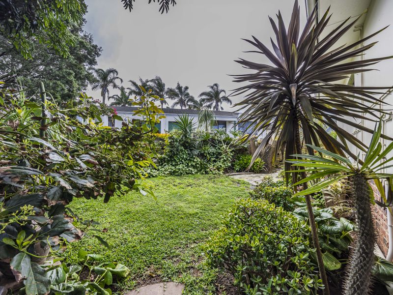 A lush, established rear garden featuring a well-maintained lawn, mature trees, and a brick boundary wall.