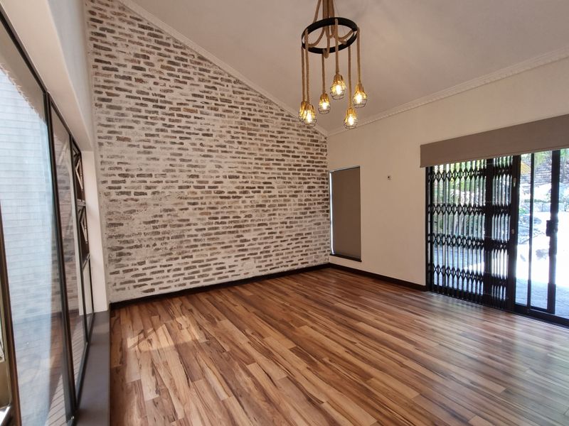 Spacious living area featuring a striking exposed brick feature wall, vaulted ceilings, and high-quality laminate wood flooring with direct access to the outdoor area.