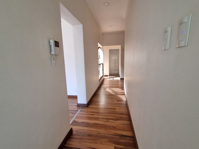A bright and clean hallway featuring warm-toned laminate flooring, recessed ceiling lighting, and a wall-mounted intercom system.