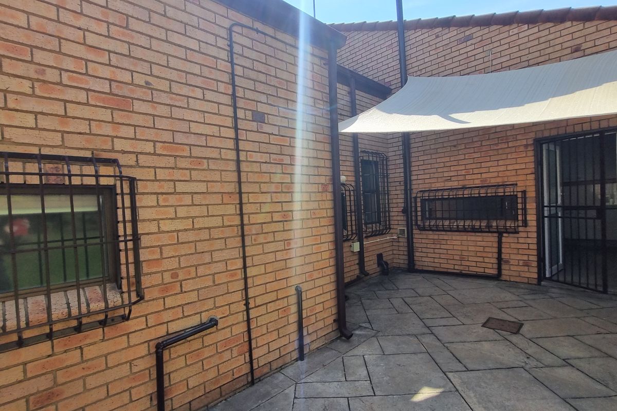 A rear exterior view featuring a paved patio area, brick walls with security bars, and a shade sail covering the outdoor space.