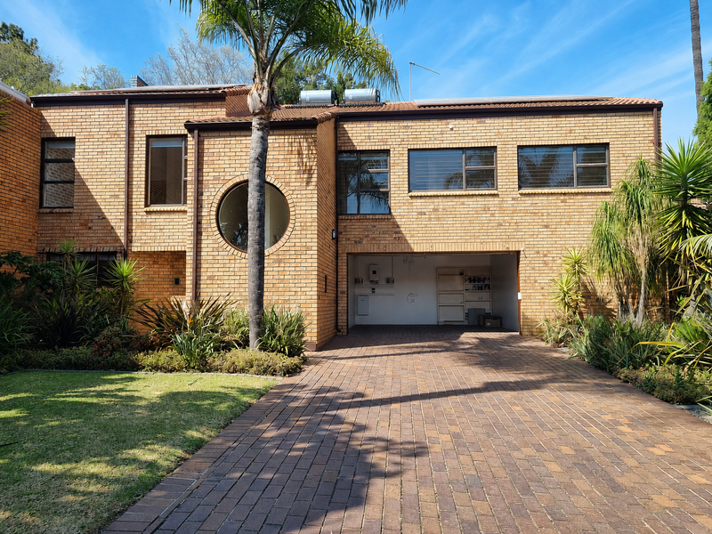 A well-maintained double-story brick residence featuring a paved driveway, integrated garage, solar water heating system, and established garden landscaping.