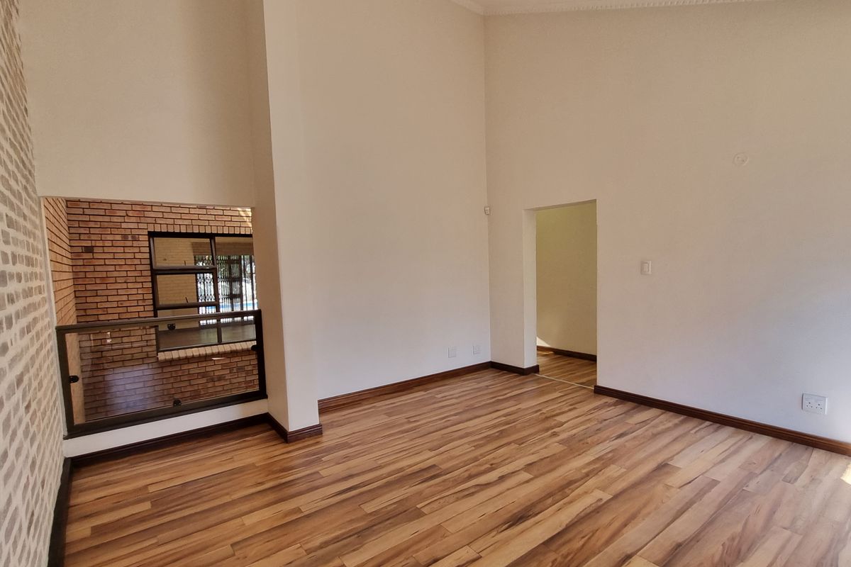 Spacious living area featuring high ceilings, laminate wood flooring, an exposed brick accent wall, and a modern glass balustrade overlooking the lower level.