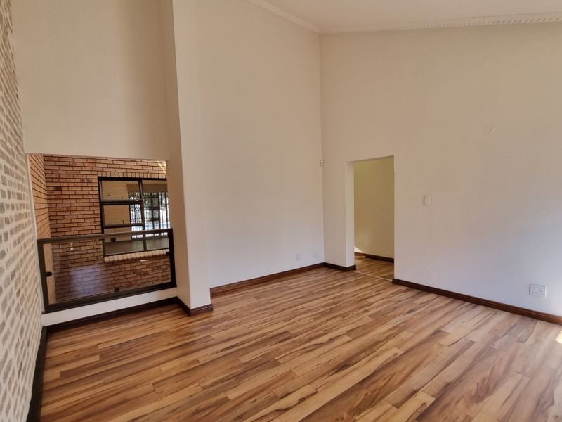 Spacious living area featuring high ceilings, laminate wood flooring, an exposed brick accent wall, and a modern glass balustrade overlooking the lower level.