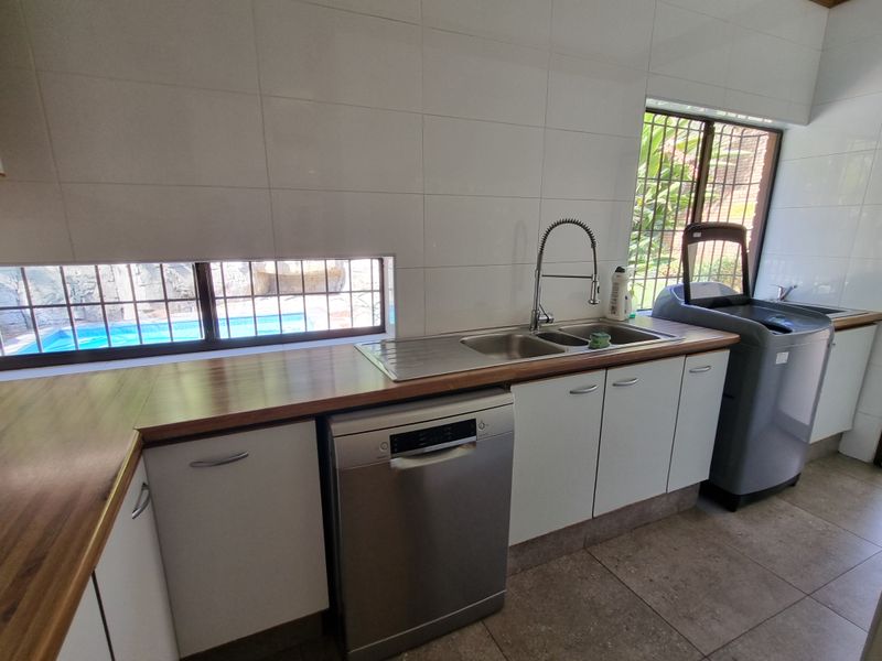 Functional laundry area featuring a stainless steel double sink, wooden countertops, ample built-in cabinetry, and tiled splashbacks with views of the pool area.