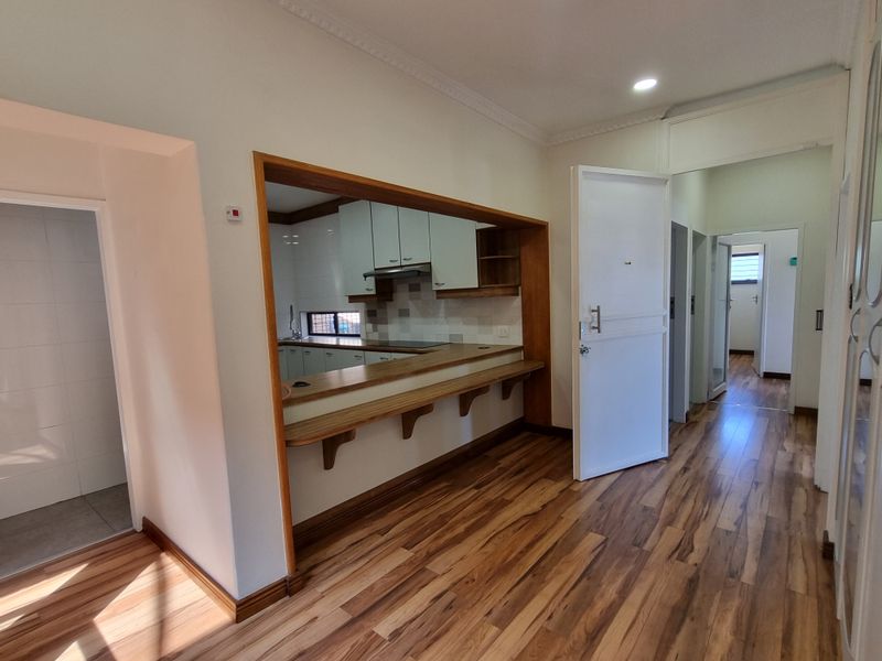 Open plan living area featuring laminate flooring, a breakfast bar pass-through to the kitchen, and neutral finishes throughout.