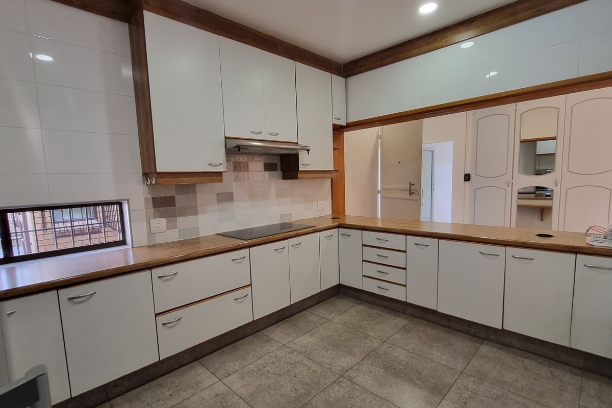 A clean, modern kitchen featuring white cabinetry, warm wooden countertops, an integrated hob with extractor, and neutral floor tiling.
