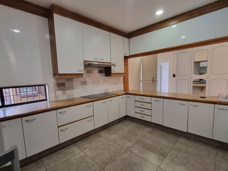 A clean, modern kitchen featuring white cabinetry, warm wooden countertops, an integrated hob with extractor, and neutral floor tiling.