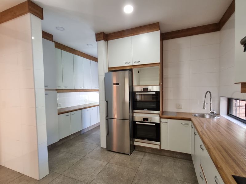Modern kitchen featuring sleek white cabinetry, warm wooden countertops, integrated double wall ovens, and high-quality tiled finishes throughout.