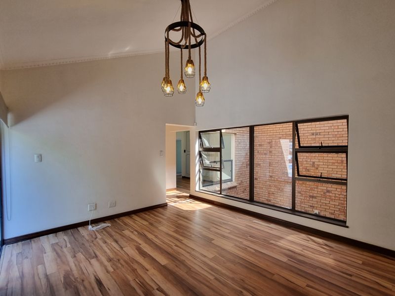 Spacious living area featuring vaulted ceilings, modern laminate flooring, and large windows that provide ample natural light.