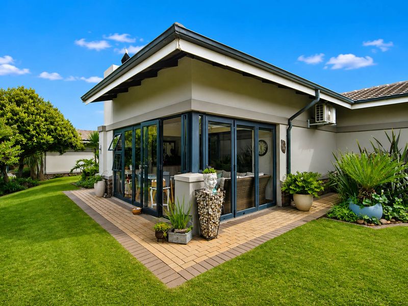 A well-maintained rear exterior view featuring a paved patio area, modern bi-fold doors, and a neatly landscaped garden.