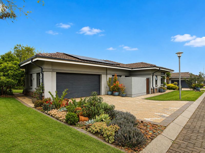 A well-maintained retirement village home featuring a paved driveway, automated garage, solar panels, and established landscaped gardens.