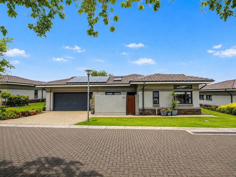 A well-maintained single-story retirement home featuring a paved driveway, integrated garage, solar panels, and attractive stone cladding accents.