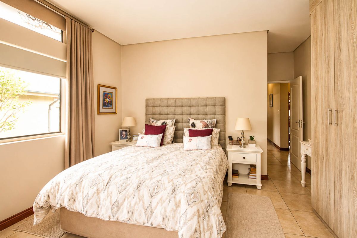 A well-maintained bedroom featuring neutral tones, tiled flooring, a large window for natural light, and integrated built-in wardrobe storage.